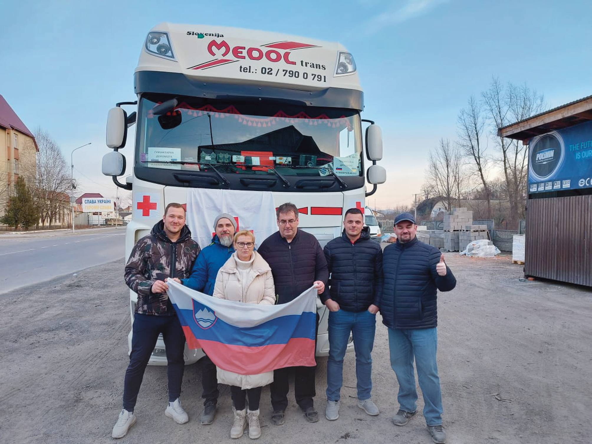 Slovenska zastava na ukrajinskih tleh. V ozadju eden od mnogih plakatov po napadeni državi: Slava Ukrajini, herojem slava!